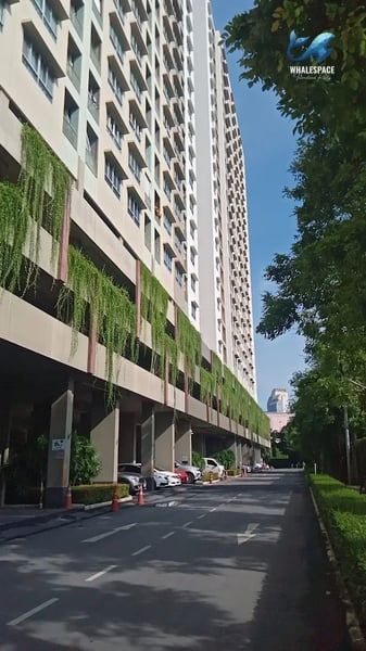 Exterior view of a high-rise condominium building with greenery cascading down its facade and a parking area.