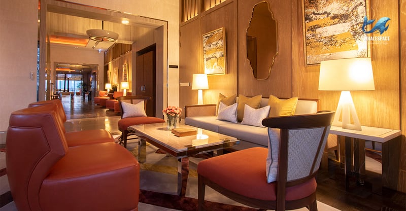 Luxurious lounge space featuring rich wooden paneling, warm ambient lighting, and plush orange and beige seating arrangements.