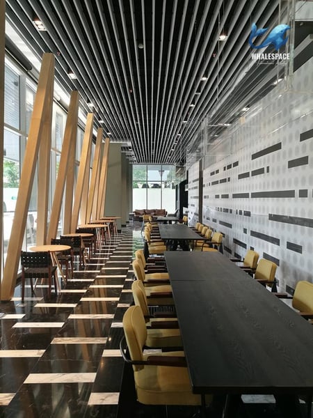 Contemporary co-working space with long communal tables, individual cafe seating, and distinctive ceiling design.