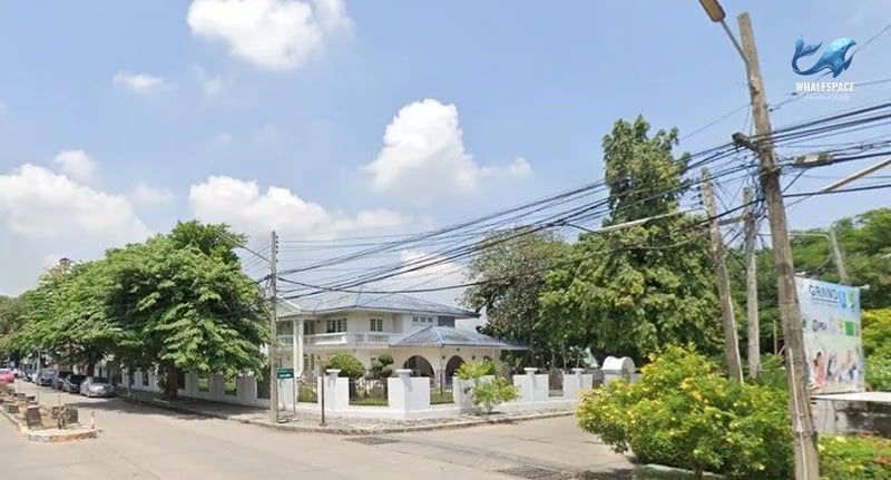 Elegant white house with a pitched roof, surrounded by mature trees and a white fence.