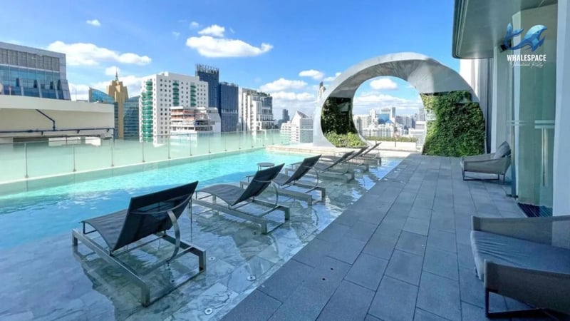 Expansive rooftop swimming pool featuring comfortable lounge chairs and a modern arch structure, set against a vibrant city skyline under a clear blue sky.