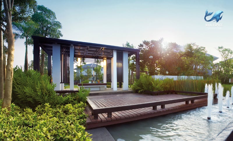 Tranquil outdoor pavilion with a wooden deck overlooking a serene water feature surrounded by lush greenery.