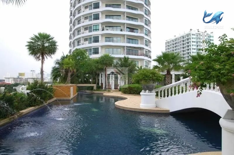 Building facade with a decorative pool area, lush greenery, and a bridge