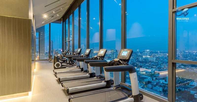 Modern fitness center equipped with treadmills and other cardio machines, offering panoramic city skyline views through floor-to-ceiling windows