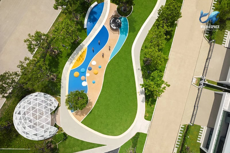 Aerial view of a vibrant children's playground and recreational path, featuring a geodesic dome and various play structures amidst green lawns.