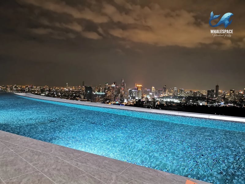 Rooftop infinity pool illuminated at night, showcasing the glittering city lights and urban skyline.