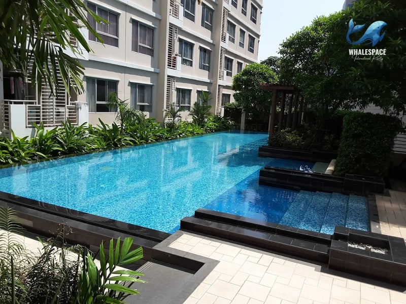 Outdoor swimming pool featuring a tiled deck and lush surrounding greenery with a residential building in the background.