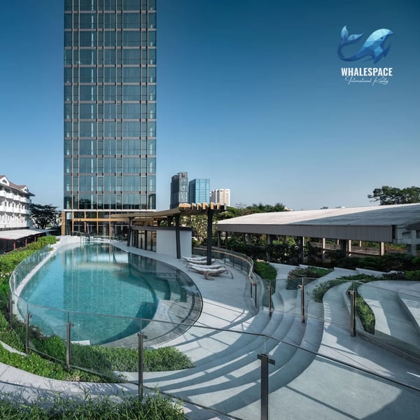 Aerial view of the large outdoor swimming pool complex with curved edges, sun loungers, and lush green landscaping surrounding the modern tower.