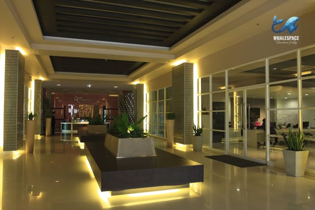 Grand and well-lit lobby with modern seating, decorative plants, and a view into a business center.