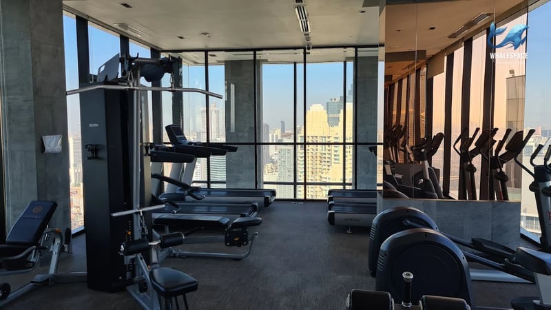 Well-equipped fitness center with treadmills, ellipticals, and weight machines, offering panoramic city views.