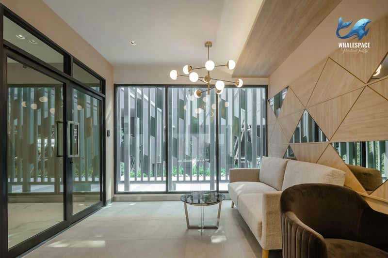 Stylish lounge area with a light beige sofa, glass coffee table, and an accent chair, featuring geometric wall paneling and a modern chandelier.