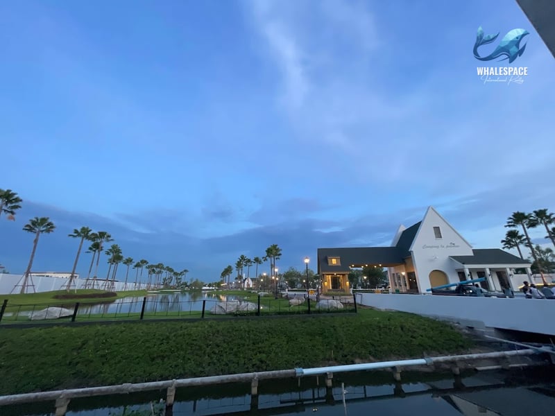 Tranquil waterside landscape with a reflection pond, manicured lawns, and scattered rocks, complemented by tall palm trees under a twilight sky.