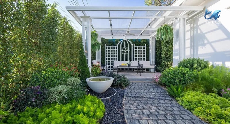Tranquil garden seating area with a water feature, surrounded by dense foliage, flowering plants, and a decorative paved pathway.