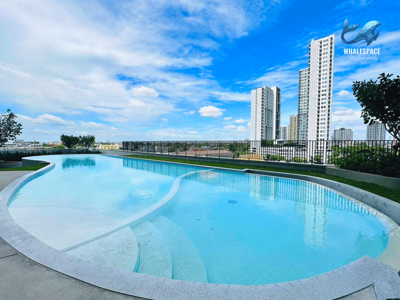 Expansive outdoor swimming pool with a unique curved design, set against a backdrop of modern high-rise buildings under a clear blue sky.