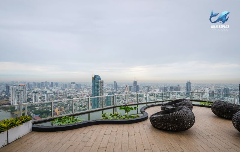 Expansive rooftop deck with comfortable wicker lounge seating, a decorative water feature, and a wide panoramic city and river view.