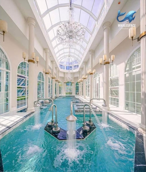 Indoor aquatic area with a grand skylight, classical columns, and various water features, providing a luxurious spa-like experience.