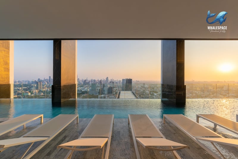 Rooftop infinity pool with lounge chairs overlooking a sprawling cityscape at sunset.