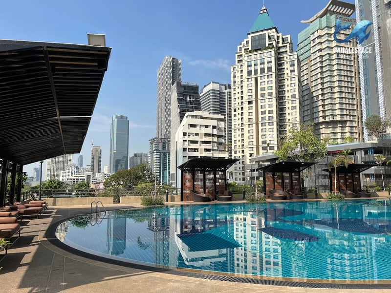Large outdoor swimming pool with inviting lounge chairs and shaded cabanas, set against a backdrop of modern city buildings.