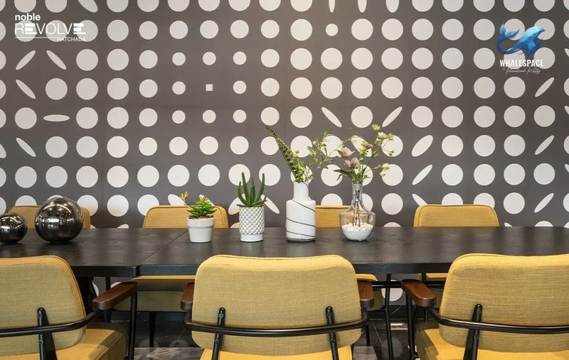 Vibrant lounge area featuring a long communal table, mustard yellow chairs, and a playful polka-dot wall design.