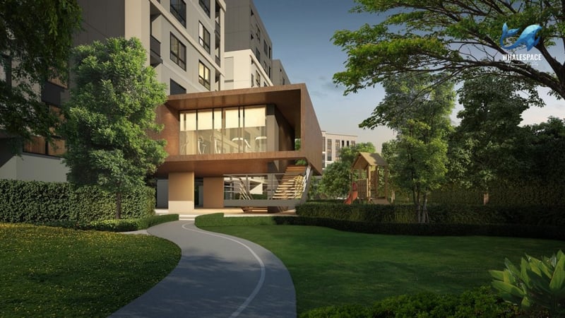 A winding pathway through a lush green garden, leading to a contemporary building that appears to house a fitness center, with a visible kids' playground nearby.