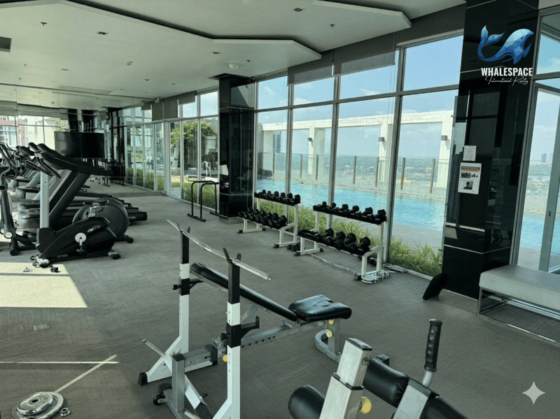 Modern fitness center with a range of exercise equipment and expansive windows overlooking a city skyline and outdoor pool area.