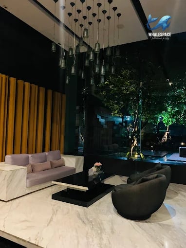Chic lounge area featuring a modern purple sofa, a dark coffee table, and ambient lighting, with views of an outdoor greenery.