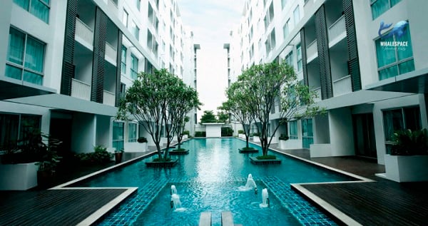 Serene rectangular pool situated between apartment buildings, featuring ornamental trees and elegant water fountains.