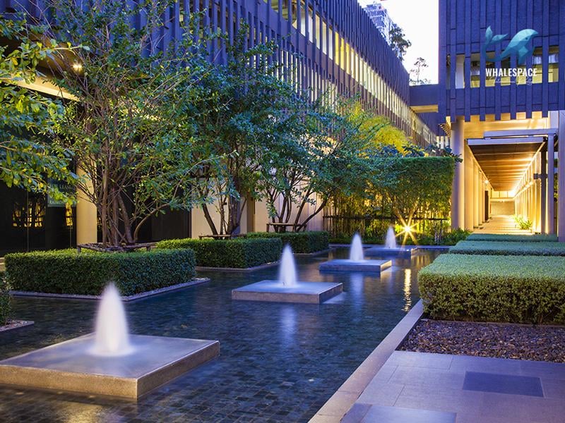 Tranquil water feature with fountains amidst manicured hedges and trees.