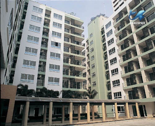 View of multiple condominium buildings with light-colored facades and green accents, featuring numerous balconies and covered walkways.