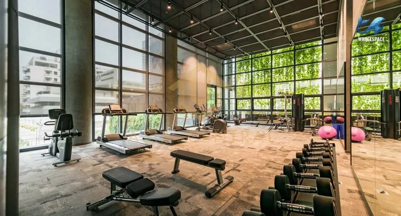 State-of-the-art fitness center with treadmills, weight machines, and free weights, featuring floor-to-ceiling windows with lush greenery views.