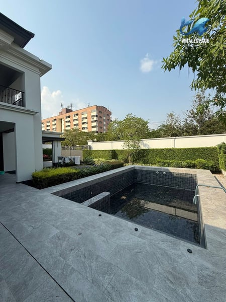 A private pool surrounded by elegant tiling and manicured hedges, with a contemporary building in the background.