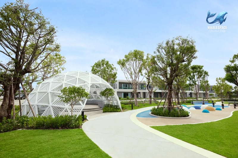 Lush green community garden with a unique geodesic dome structure and colorful children's play area elements, surrounded by mature trees.