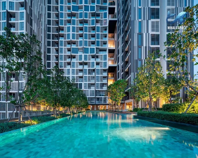 Expansive swimming pool with mosaic tiles and surrounding lush greenery, illuminated for evening ambiance.