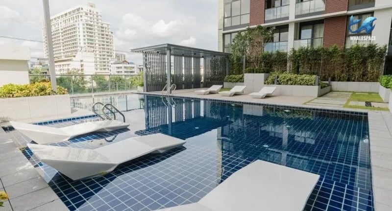Resort-style swimming pool with modern lounge chairs and lush landscaping, offering a serene oasis with city views.