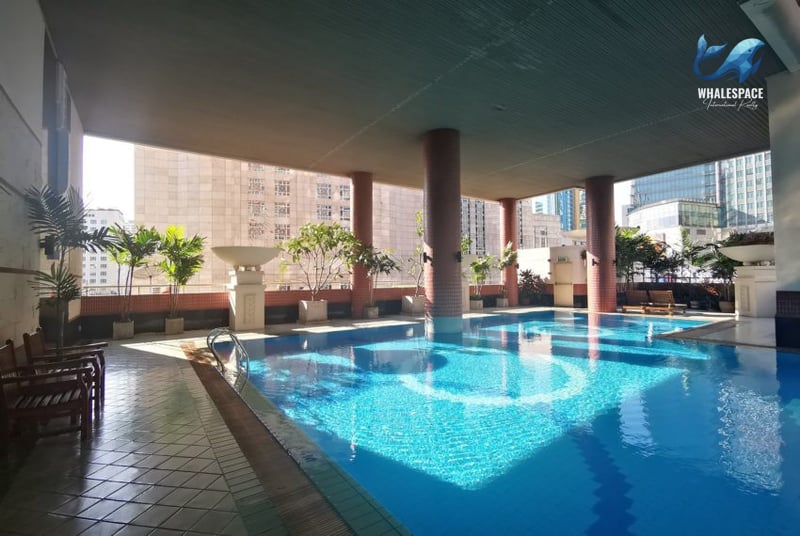 Spacious swimming pool surrounded by lush greenery and comfortable chairs.