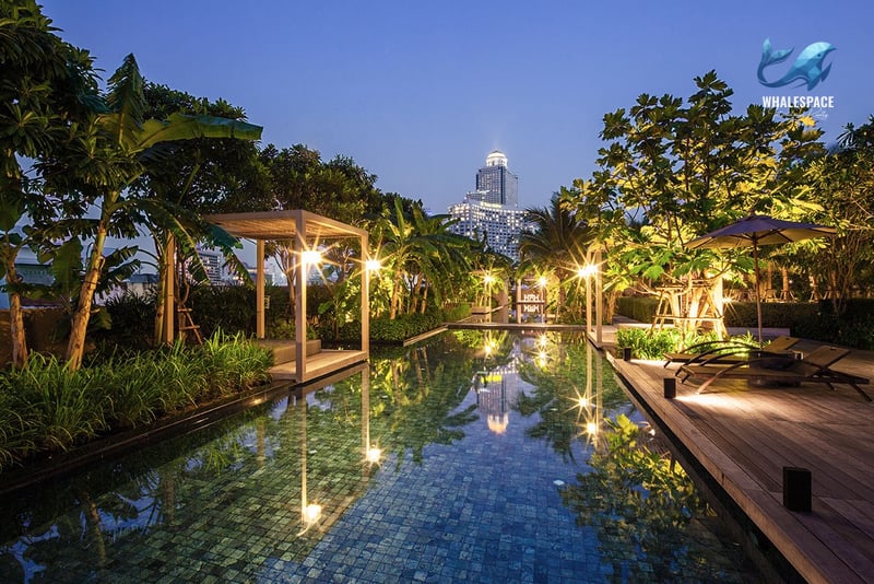 Serene swimming pool area surrounded by lush tropical landscaping and ambient lighting.