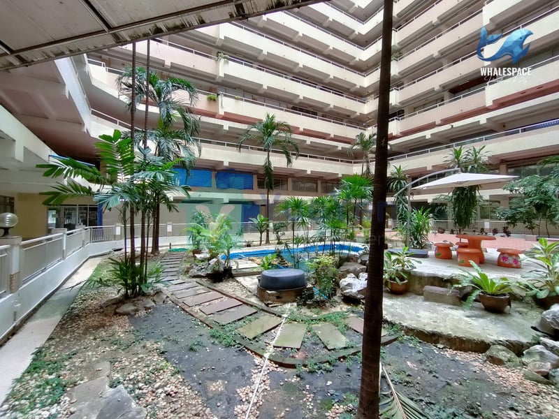 Central courtyard with a small pond, stepping stones, and lush greenery, surrounded by building floors.