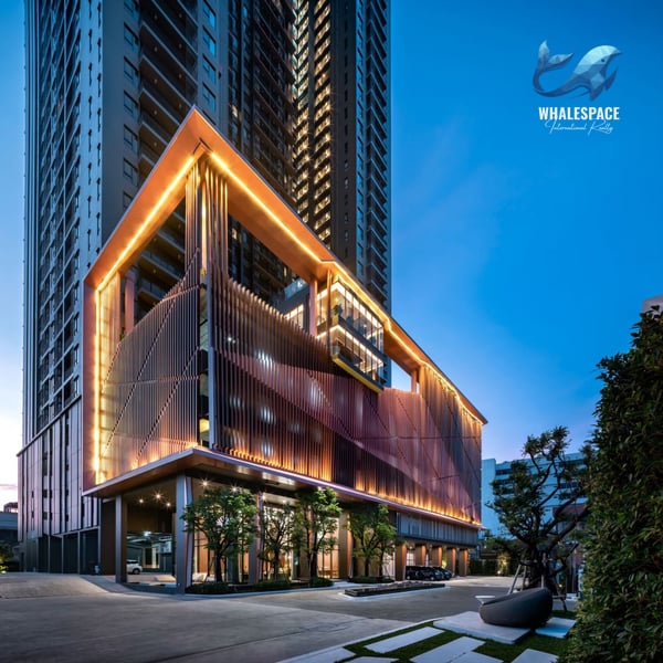Modern condominium facade with illuminated architectural details and lush landscaping at dusk