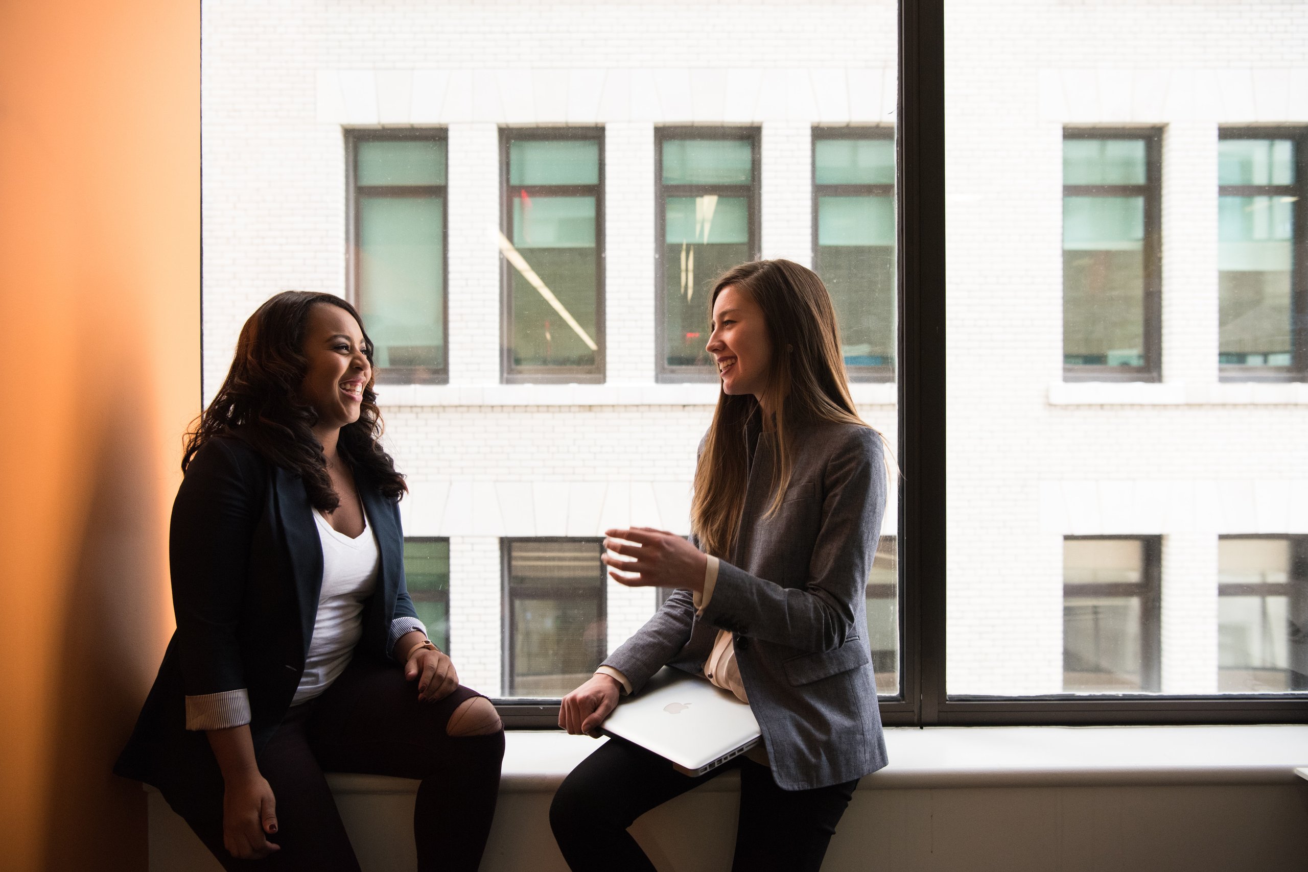 Two people in conversation, seated in front of an office window