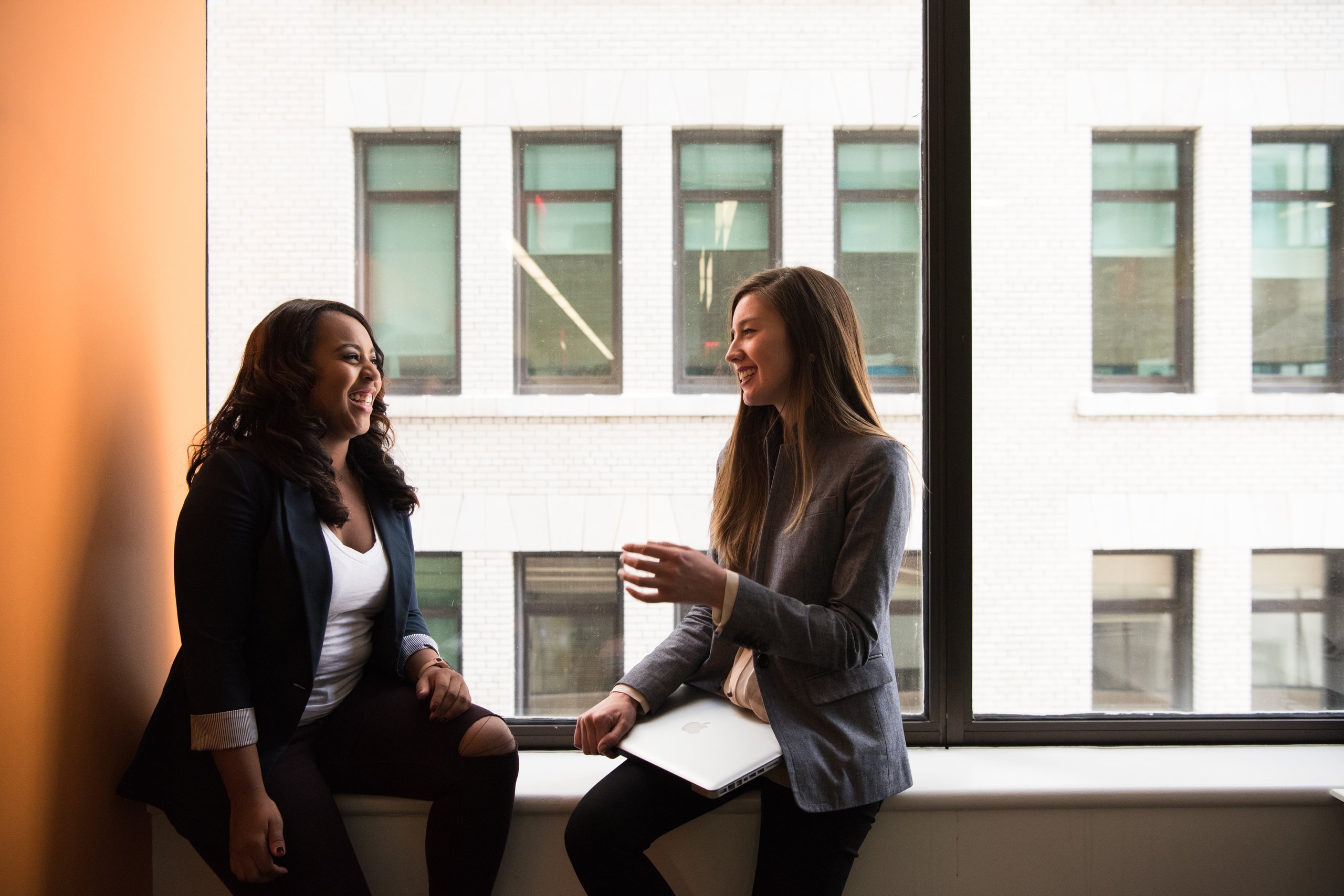 wo people in conversation, seated in front of an office window