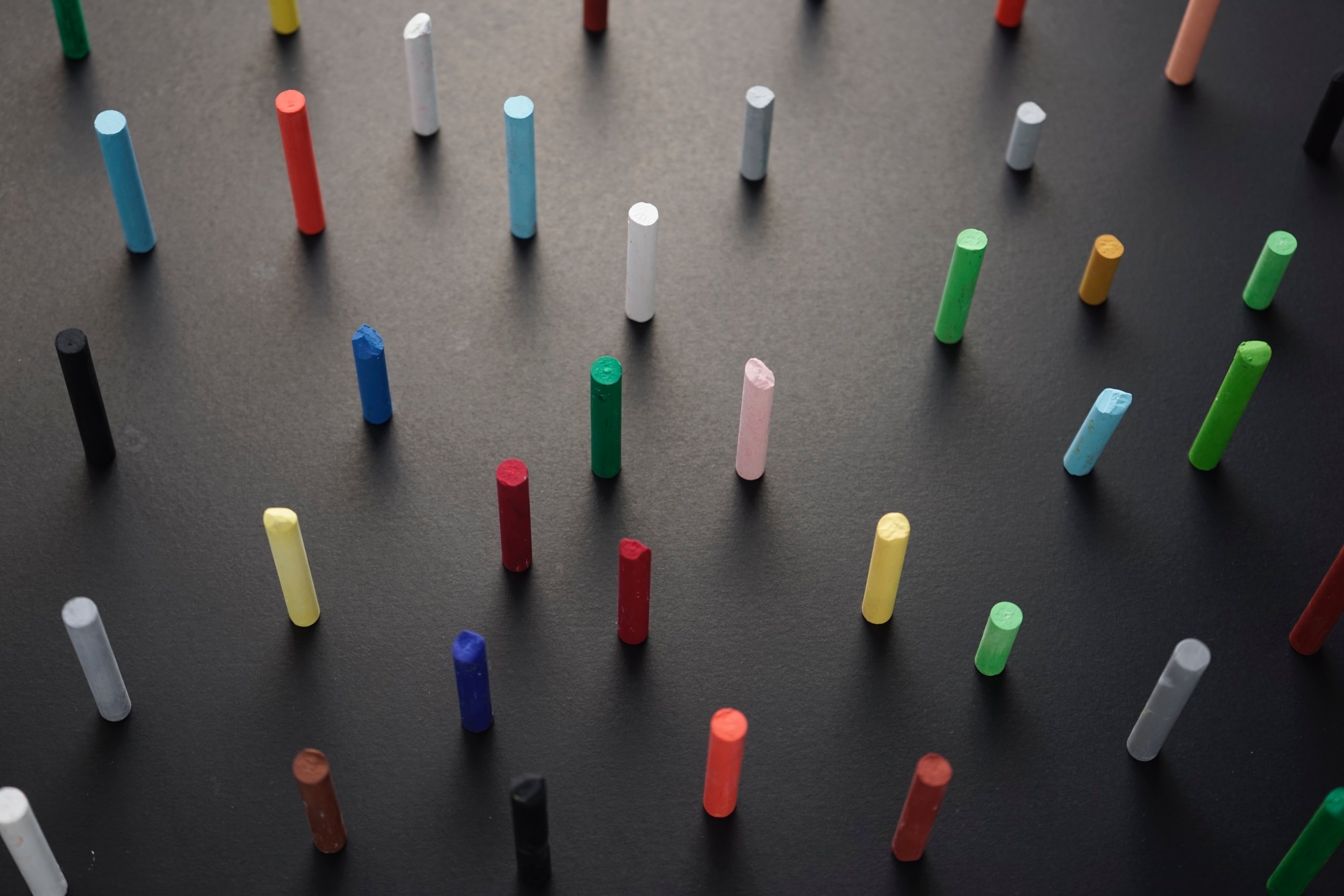 Chalk pastel crayons placed upright on a dark grey surface.