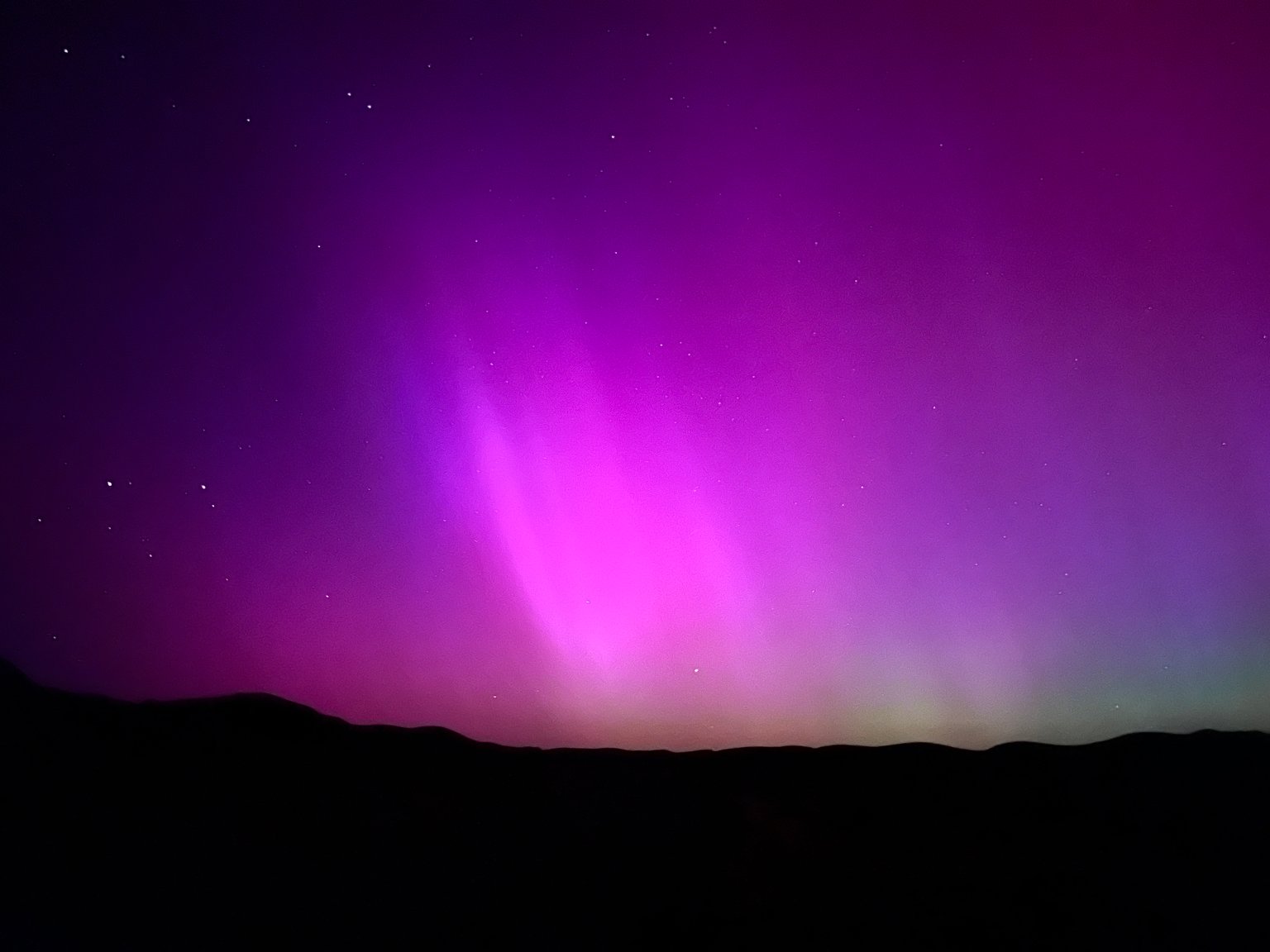 Růžovofialové paprsky polární záře nad tmavými kopci v Nevadě, vyfotografované iPhonem 13 Pro.