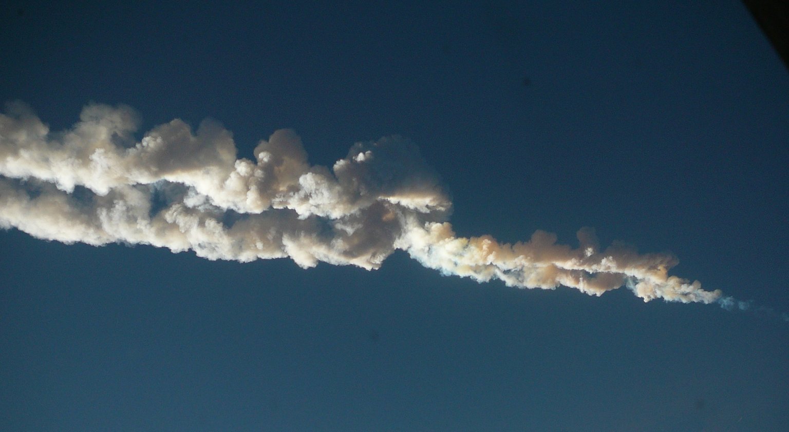Dvojitá světlá stopa čeljabinského meteoru na modré obloze.