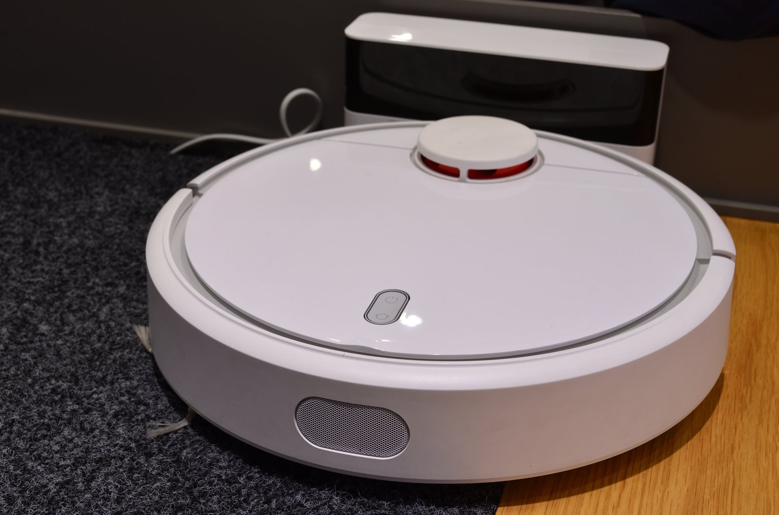 Xiaomi Mi Robot Vacuum u nabíjecí stanice s viditelnými tlačítky napájení a návratu domů.