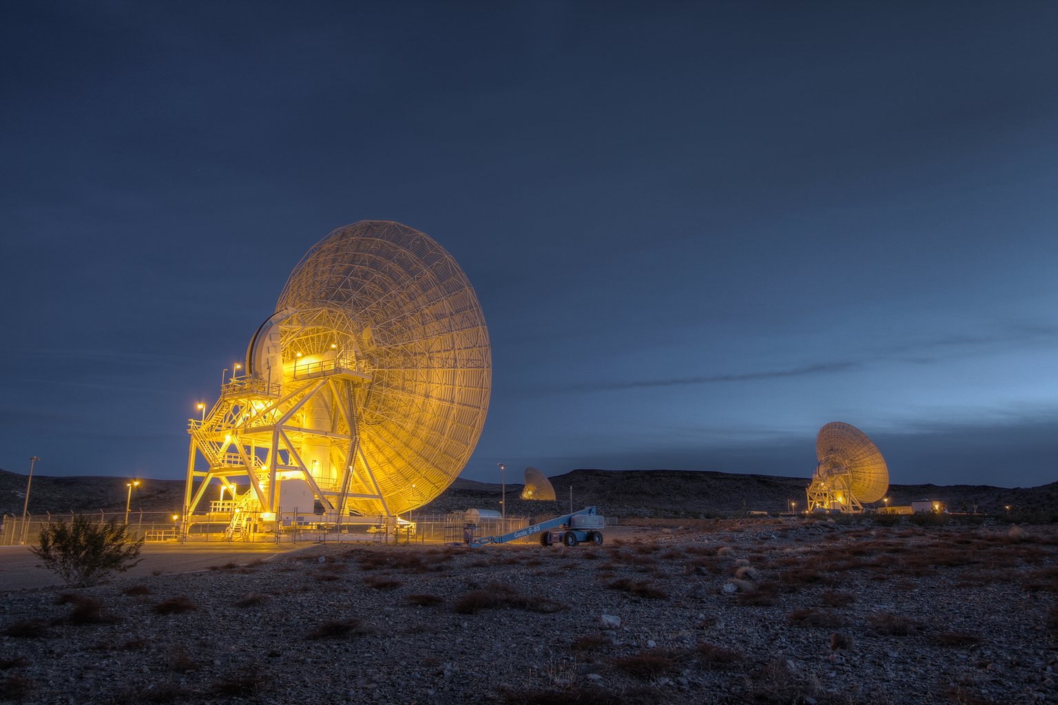 Osvětlené parabolické antény sítě Deep Space Network v Goldstone za soumraku.