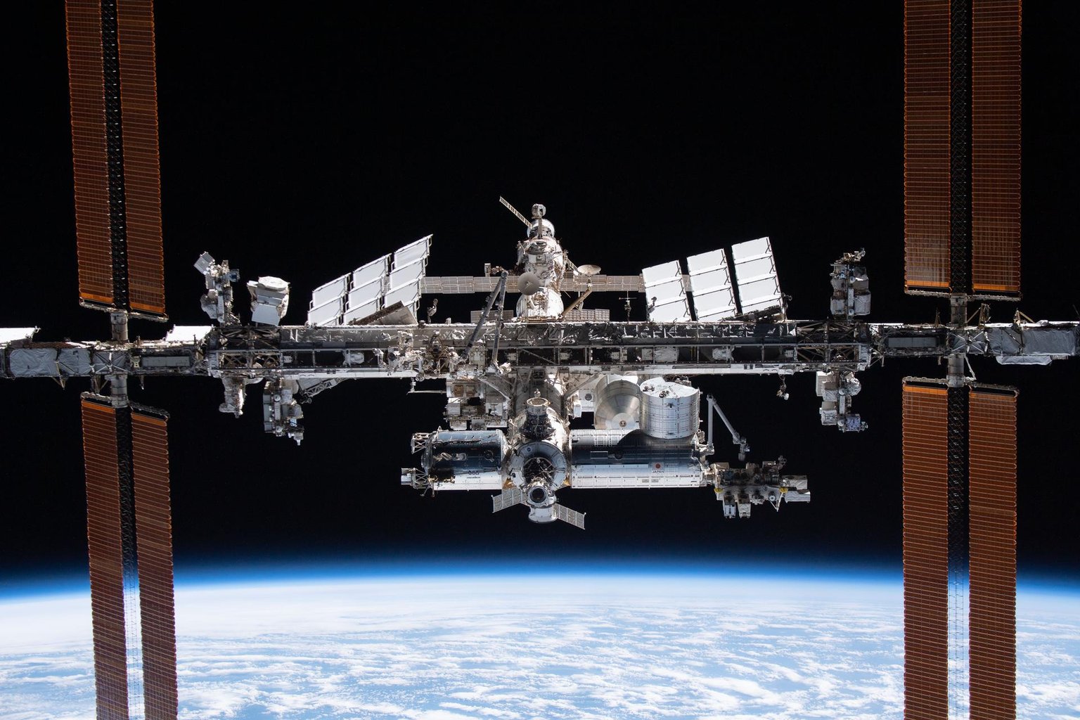 ISS s rozvinutými solárními panely nad zakřiveným zemským obzorem