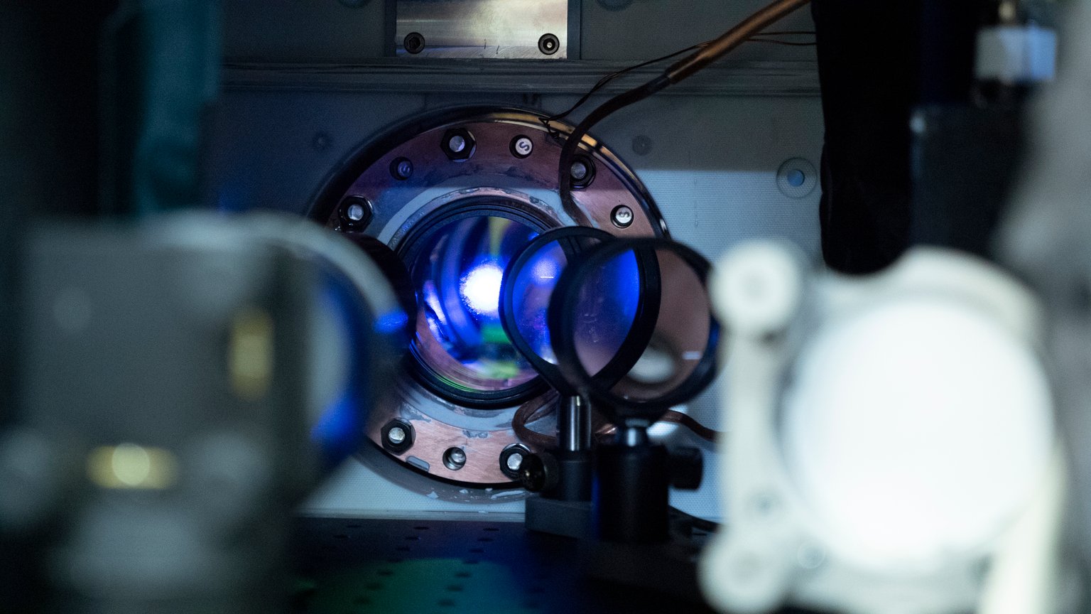 Modře zářící atomový vzorek v kruhovém průzoru aparatury atomových hodin JILA.