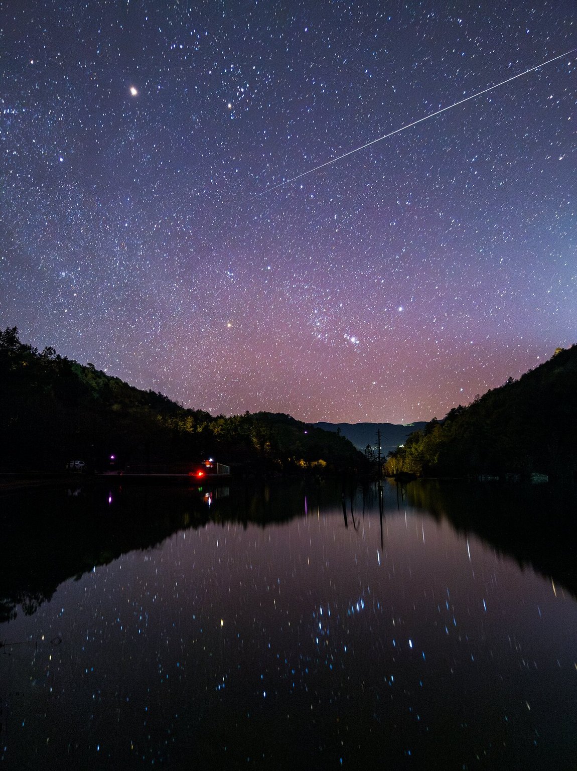 Jasná Geminida nad údolím Blue Moon Valley v Číně a hvězdy odražené na hladině.