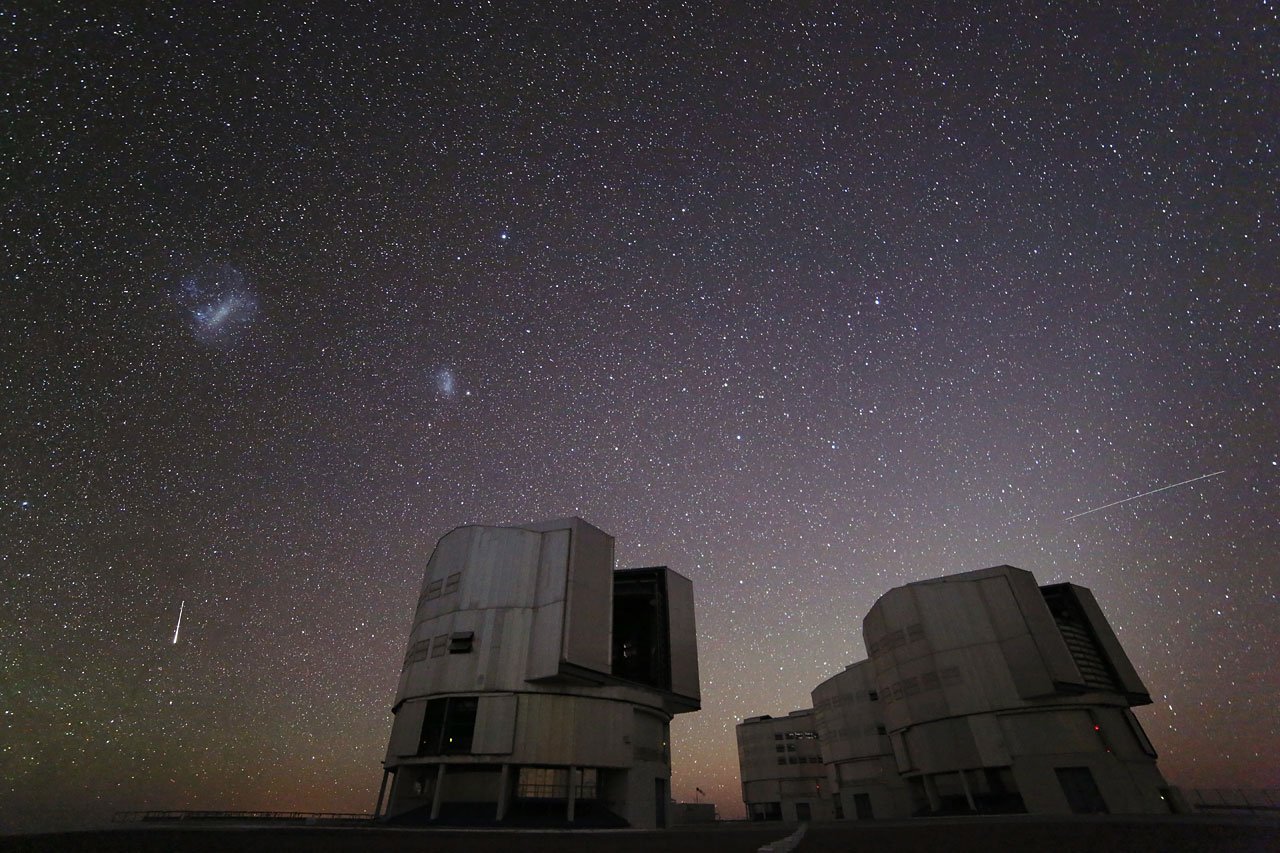 Meteorické stopy nad budovami observatoře Paranal pod hvězdnou oblohou.