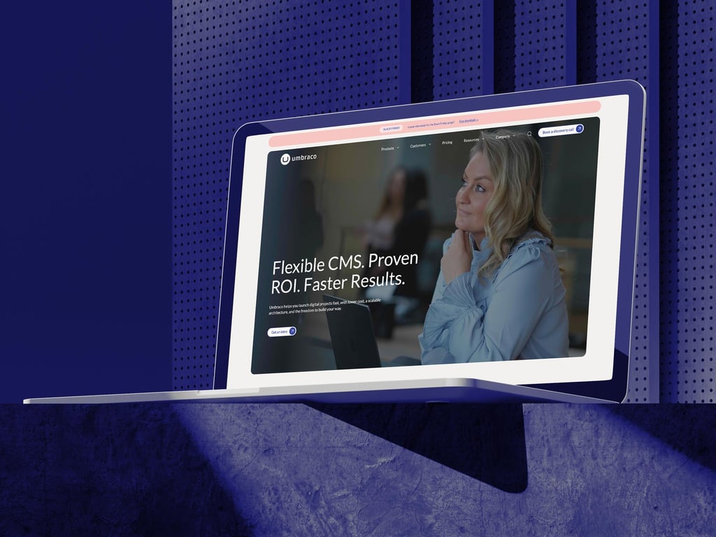 A laptop sits on a blue textured surface displaying a website with a woman thinking, and the text “Flexible CMS. Proven ROI. Faster Results.” The background features a perforated blue wall—perfectly capturing the power of Umbraco CMS.